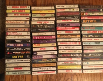 May include: A collection of vintage cassette tapes, featuring a variety of music genres. The tapes are stacked together, with titles and artist names visible. The labels display a range of colors and fonts, showcasing music from the 80s and 90s.