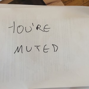 Puede incluir: Una pila de hojas de papel blanco con las palabras YOU'RE MUTED escritas en tinta negra en la página superior. El texto está escrito a mano en letras mayúsculas, con la palabra YOU'RE en la primera línea y la palabra MUTED en la segunda.
