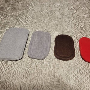 May include: Four felt pads in a row, each with a rounded rectangular shape. The pads are in shades of gray, brown, and red. The pads are arranged on a patterned, quilted surface.