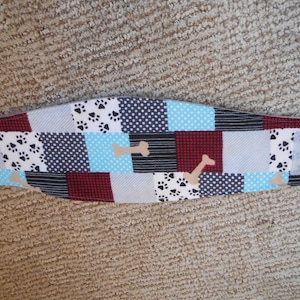 May include: A patchwork fabric dog collar with a blue, white, and red color scheme. The collar features paw prints and bone designs.