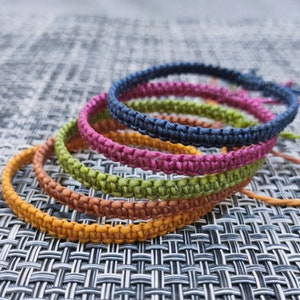 May include: Four colorful braided bracelets stacked on top of each other. The bracelets are in shades of orange, green, pink, and blue.