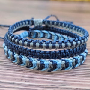 May include: Three braided bracelets in shades of blue and gray. The bracelets are made with a woven knot pattern.