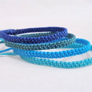 May include: Four braided bracelets in shades of blue, from dark blue to light blue, stacked on a white surface.