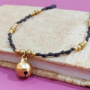 May include: A black cord bracelet with gold beads and a gold bell charm.