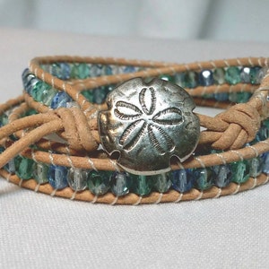 May include: Wrap bracelet with blue and green beads, tan leather, and a silver-tone sand dollar button clasp. The bracelet wraps multiple times around the wrist.