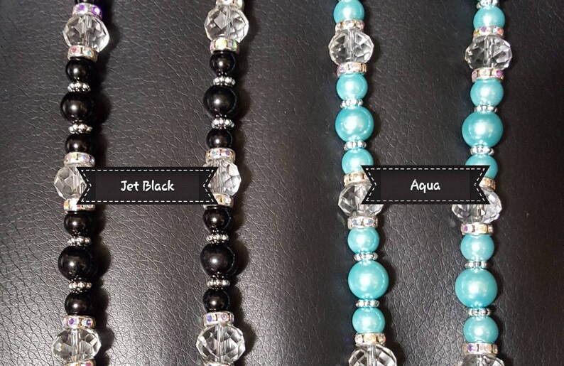 K&ouml;nnte beinhalten: Zwei Perlenketten, eine schwarze und eine aquablau, mit klaren Kristallperlen und silbernen Akzenten. Die Ketten sind mit "Jet Black" und "Aqua" beschriftet.