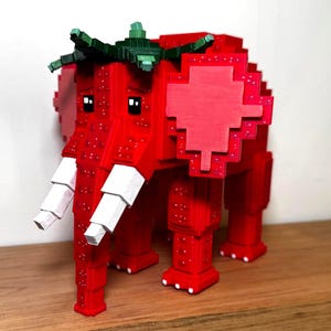 Pode incluir: Uma escultura de elefante vermelho pixelizado com presas brancas e detalhes verdes em forma de folha. O corpo do elefante é vermelho vibrante, com um design de morango. Um item decorativo único.