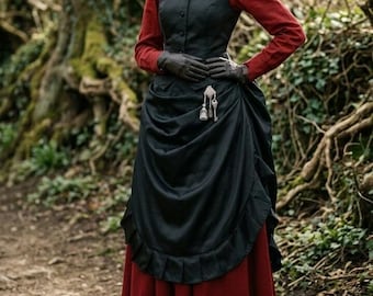 May include: A long-sleeved red blouse with a high collar, a black button-down vest, and a black overskirt with a ruffled hem. The outfit includes a long red skirt with a ruffled bottom, black leather gloves, a black beaded necklace, and a silver brooch.