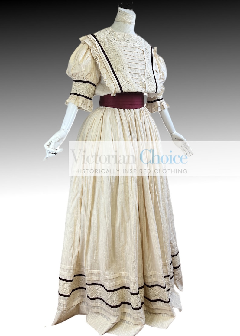 Pode incluir: Um vestido branco de algod&atilde;o com decote alto e mangas bufantes. O vestido tem uma faixa bord&ocirc; e detalhes pretos. O vestido &eacute; de estilo vitoriano e inspirado historicamente.