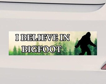 Puede incluir: Una pegatina para parachoques verde y marrón con el texto "I believe in Bigfoot" y una silueta de Bigfoot caminando por un bosque.