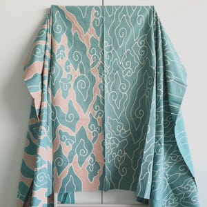 Könnte beinhalten: Ein türkis- und rosafarbenes Gewebe mit einem weißen Wirbelmuster. Der Stoff ist über einem weißen Gestell drapiert, das das komplizierte Design zeigt. Das Muster weist organische Formen und Linien auf und erzeugt eine fließende Ästhetik.