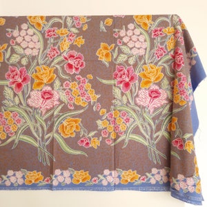 May include: A brown fabric with a floral pattern featuring pink, yellow, and white flowers on a brown background. The fabric has a blue border.
