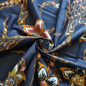 May include: A close-up of a dark blue fabric with a repeating pattern of stylized flowers in shades of orange, yellow, white, and red. The fabric is folded and draped, showcasing the intricate design.