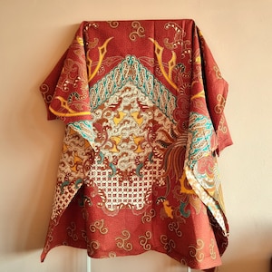 Könnte beinhalten: Ein roter, gelber und grüner gemusterter Stoff mit einem floralen Design. Der Stoff hat einen Fransenrand und ist über einen Kleiderbügel gelegt.