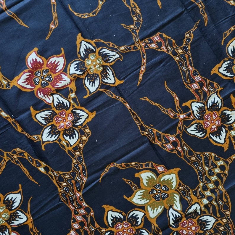 May include: Black fabric with a repeating pattern of stylized flowers in shades of orange, red, white, and green. The flowers are arranged on a dark blue background with intricate branches.