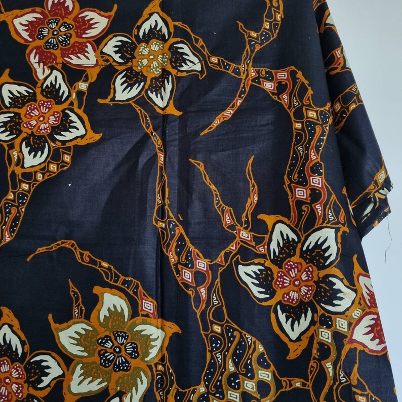 May include: Black fabric with a repeating pattern of stylized flowers in shades of orange, yellow, white, and red. The flowers are outlined in white and have a black center. The background is a dark blue.