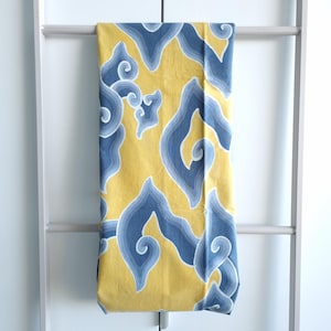 Könnte beinhalten: Ein gelbes Textil mit einem sich wiederholenden blau-weißen wolkenartigen Muster. Der Stoff ist über eine weiße Leiter drapiert, wodurch die komplizierten Details des Designs zur Geltung kommen. Das Textildesign weist wirbelnde, organische Formen auf.