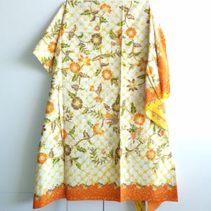 Peut inclure: Un tissu blanc avec un motif floral jaune et orange. Le tissu a une bordure orange et jaune.