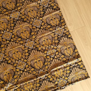 Op de afbeelding: Zwarte stof met een gouden en wit bloemenpatroon. De stof heeft een herhalend patroon van gestileerde bloemen en bladeren.