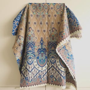 Può includere: Un tessuto fantasia con sfondo marrone e disegni floreali blu e turchese. Il tessuto ha un bordo beige con un bordo a zig-zag. Il tessuto è piegato, mostrando il motivo e il design.