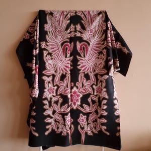 Può includere: Tessuto nero con un motivo floreale rosa e bianco con due uccelli. Il tessuto ha un design batik tradizionale.