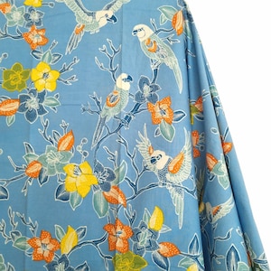Può includere: Tessuto blu con un motivo ripetitivo di pappagalli e fiori. I pappagalli sono bianchi, grigi e arancioni. I fiori sono arancioni, gialli e bianchi.