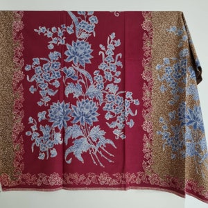 Könnte beinhalten: Ein roter und brauner Stoff mit einem Blumenmuster. Die Blumen sind blau und weiß und haben ein zartes Design. Der Stoff hat einen Rand aus kleinen weißen Blumen.