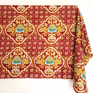 Può includere: Tessuto rosso con un motivo floreale bianco e oro. Il motivo presenta un disegno ripetitivo di fiori stilizzati con centri blu.