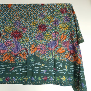 Op de afbeelding: Teal stof met een kleurrijk batikpatroon met gestileerde vogels, bloemen en bladeren. Het patroon doet denken aan traditionele Indonesische batik.