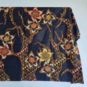 Op de afbeelding: Zwarte stof met een bloemenpatroon in tinten oranje, geel en rood. De stof heeft een herhalend ontwerp van gestileerde bloemen en takken.