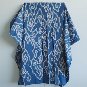 Könnte beinhalten: Ein blaues Batik-Stoffkleidungsstück mit einem weißen und grauen wolkenartigen Muster. Das Kleidungsstück hat weite Ärmel und eine lockere Passform. Der Stoff ist gefaltet und zeigt das komplizierte Design.