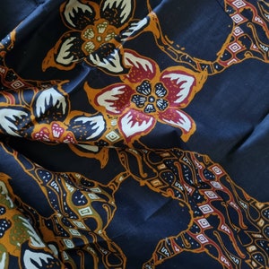 May include: A dark blue fabric with a repeating pattern of stylized flowers in shades of red, white, and yellow. The flowers have a traditional batik design.