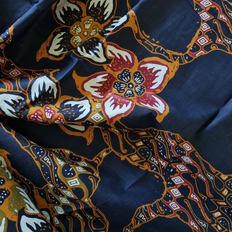 May include: A dark blue fabric with a repeating pattern of stylized flowers in shades of red, white, and yellow. The flowers have a traditional batik design.