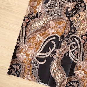 Puede incluir: Tela negra y marrón con un patrón de paisley. La tela tiene un diseño tradicional con detalles intrincados.