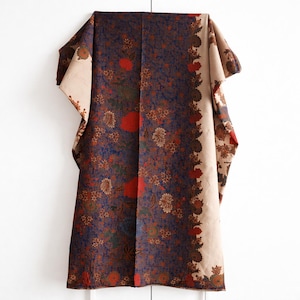 Peut inclure: Un textile plié avec un motif floral. Le tissu présente un fond bleu foncé avec des motifs floraux rouges, marron et verts. Une bordure beige avec un motif floral longe un bord. Le textile est probablement une écharpe ou un châle.