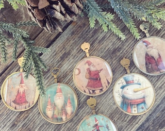May include: A collection of six vintage-style Christmas ornaments with gold-colored metal frames. Each ornament features a different festive illustration, including Santa Claus, a snowman, and a dancing figure. The ornaments are arranged on a rustic wooden surface.
