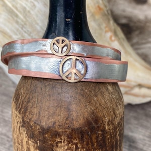 May include: Two silver and copper bracelets with peace sign charms. The bracelets are stacked on top of each other.
