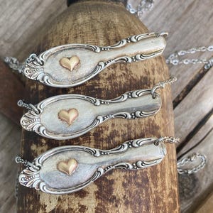 Peut inclure: Trois cuillères en argent avec des cœurs en or attachés à des chaînes. Les cuillères ont des motifs ornés et sont suspendues à une surface en bois.