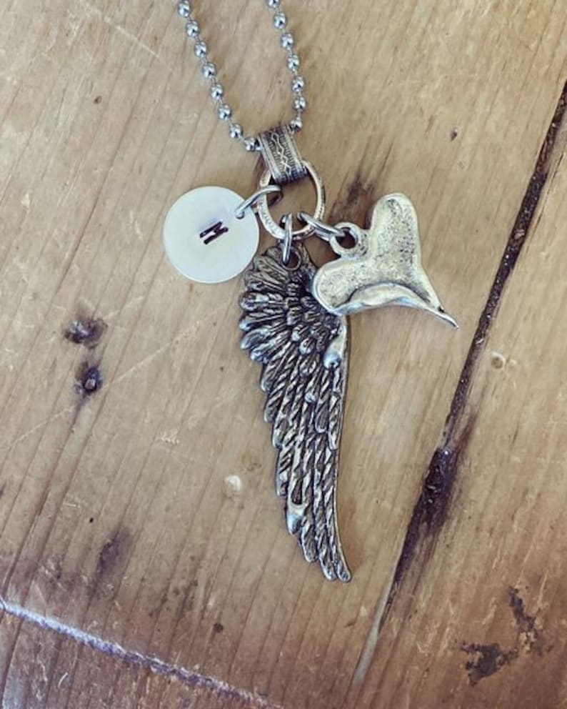 May include: Silver necklace with a heart charm, a wing charm, and a round charm with the letter 'M' on it.