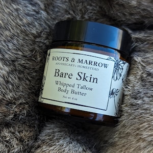 May include: A glass jar with a black lid containing a whipped tallow body butter. The label reads "ROOTS & MARROW APOTHECARY HOMESTEAD Bare Skin Whipped Tallow Body Butter Net wt. 4 oz".