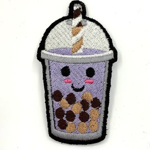 May include: A purple and white embroidered patch of a boba tea cup with a brown and white straw. The cup has a smiling face with pink cheeks and brown eyes. The cup is filled with brown and beige boba pearls.