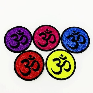 May include: Five round fabric patches with a glittery finish. Each patch features a black Om symbol on a different colored background: purple, pink, blue, red, and yellow.