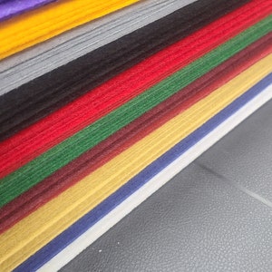 May include: A stack of colorful felt sheets in various shades of purple, yellow, gray, black, red, green, brown, gold, blue, and white.