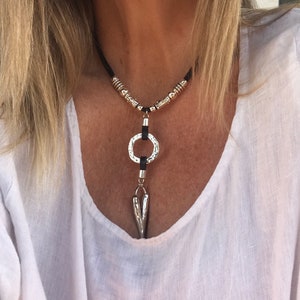 Könnte beinhalten: Eine silberne und schwarze Halskette mit einem runden Anhänger und einer spitzen Spitze. Die Halskette besteht aus Lederband und hat silberne Perlen.