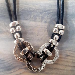 May include: A black leather necklace with three strands and silver-toned metal circles and beads.