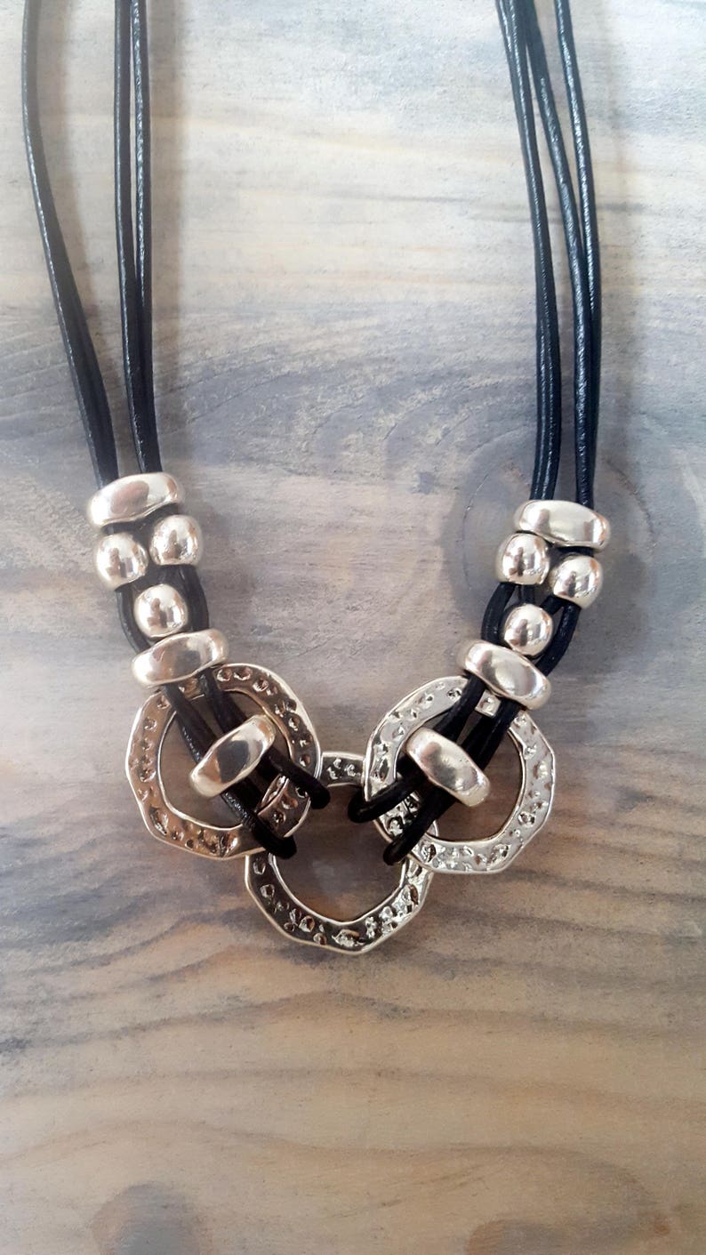May include: A black leather necklace with three strands and silver-toned metal circles and beads.