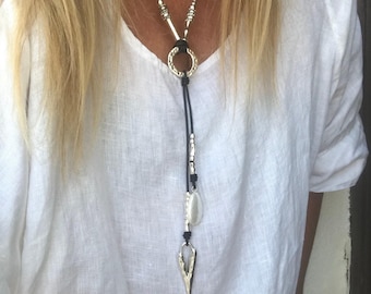 May include: A long silver necklace with a circle pendant, a white oval pendant, and a silver arrow pendant. The necklace is made of black leather cord and silver beads.