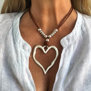 Può includere: Una collana in corda di cuoio marrone con perline d'argento e un grande ciondolo a forma di cuore d'argento.