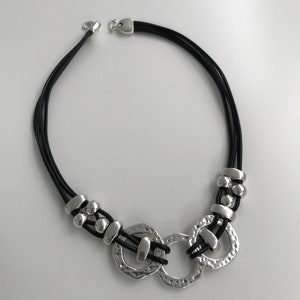 May include: A silver and black necklace with a multi-strand leather cord and a large silver pendant featuring three interlocking circles.