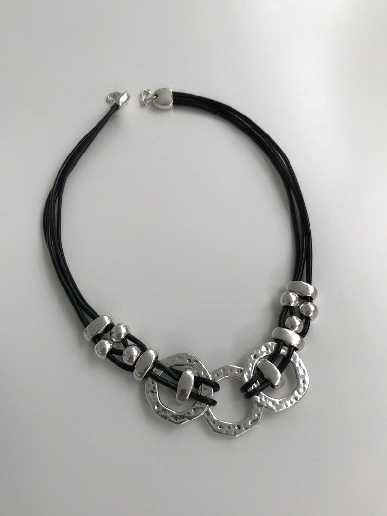 May include: A silver and black necklace with a multi-strand leather cord and a large silver pendant featuring three interlocking circles.
